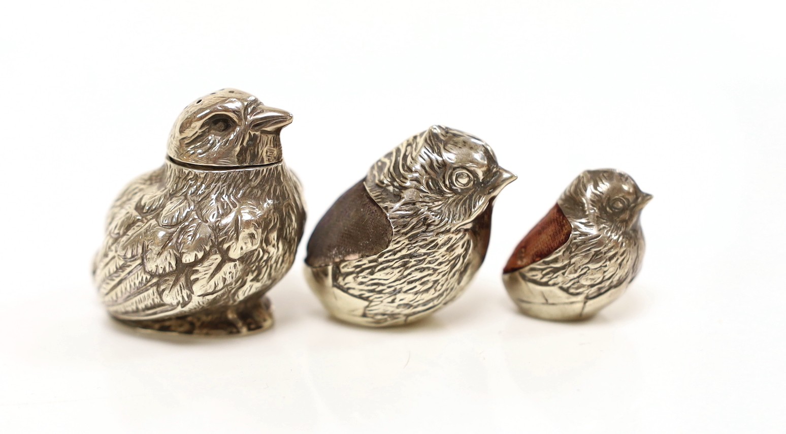 Two Edwardian silver mounted novelty pin cushions, modelled as hatching chicks, by Sampson Mordan & Co, Chester, 1906 & 1908, tallest 27mm, together with a similar novelty chick pepperette, same maker, Sheffield, 1906.